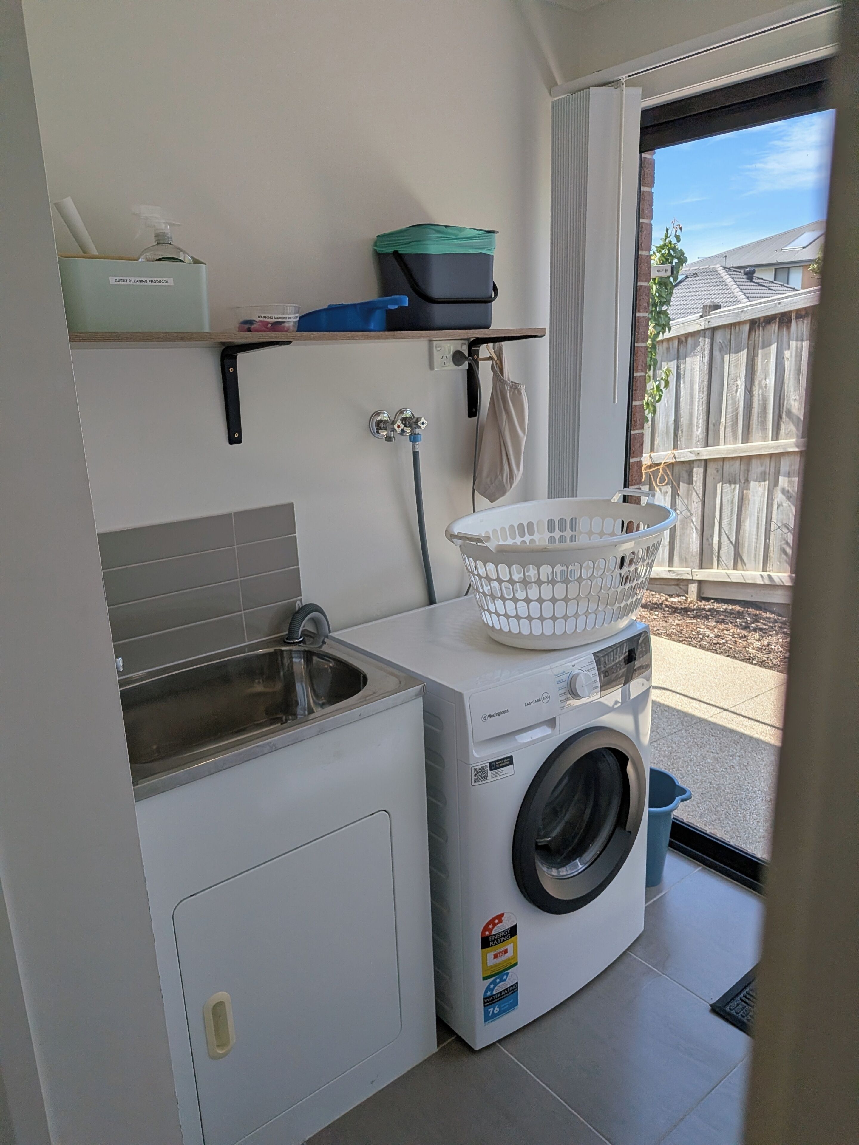 A compact laundry area with a washing machine, a sink, and a drying rack.