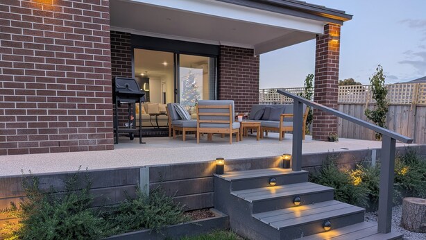 Une terrasse moderne avec un espace salon extérieur, un escalier et un mur en briques.