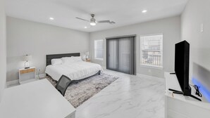 A modern bedroom with a bed, desk, chair, and a TV. - Elegant Modern Retreat • Sleeps 6 • Near NRG (Houston)