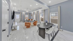 A modern living room with a sofa, coffee table, and dining area with chairs. - Elegant Modern Retreat • Sleeps 6 • Near NRG (Houston)