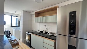 A modern kitchen with a stainless steel refrigerator, a built-in oven, and a sink. There is a window providing natural light and a view of the outside. - Ocean View on the 20th Floor | Rooftop with Jacuzzi | 1 Block from the Beach | (Maceió)