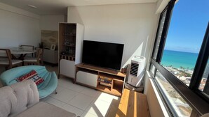A modern living room with a flat-screen TV, a sofa, a dining area, and a view of the ocean. - Ocean View on the 20th Floor | Rooftop with Jacuzzi | 1 Block from the Beach | (Maceió)