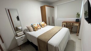 Une chambre à coucher comprenant un lit, une table de chevet, une commode, un bureau, une chaise et une plante en pot.