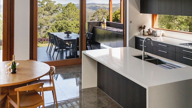 A modern kitchen with a large island, a dining area with a table and chairs, and a view of a lush landscape through large windows. - The Haven Montville, is a place of peace, a refuge crowned, 
wrinkles fade & ... (Montville)