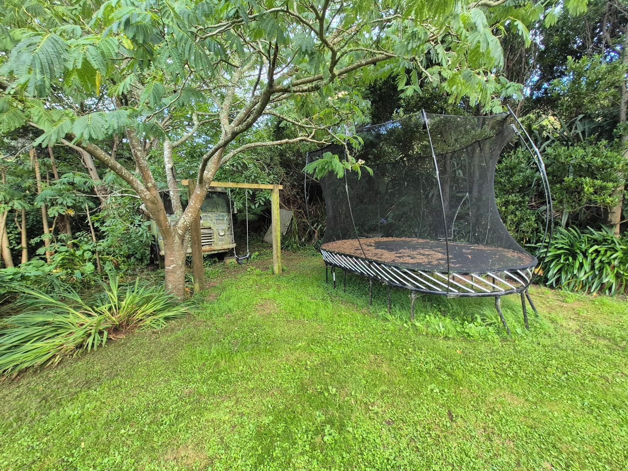 Un trampolino circondato da vegetazione rigogliosa e una casetta sugli alberi.