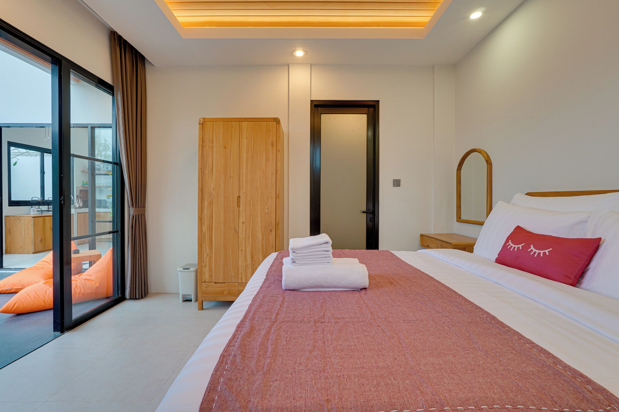 Une chambre d’hôtel moderne avec un grand lit, une armoire en bois, un miroir et une vue sur l’extérieur grâce à une porte vitrée.