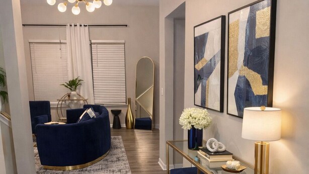 Un salon moderne avec un canapé bleu, une table basse en verre et une console dorée agrémentée d’objets décoratifs.