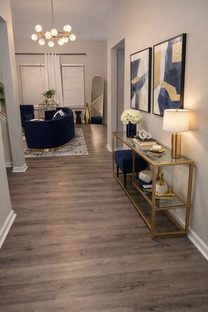Een moderne woonkamer met een blauwe bank, een glazen salontafel en een gouden console met decoratieve objecten.