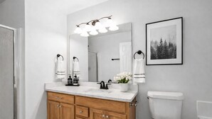 Une salle de bain moderne avec un meuble-lavabo en bois, des accessoires blancs et un tableau encadré au mur.