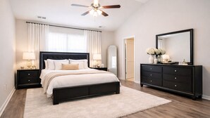 Une chambre à coucher comprenant un lit, des tables de chevet, une commode, un ventilateur de plafond et un grand miroir.