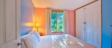 A bedroom with a bed, a window with curtains, a lamp, and a wardrobe.