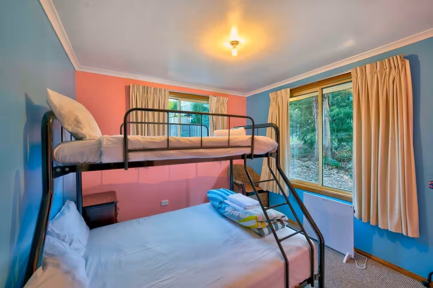 A bunk bed room with a window and curtains, a radiator, and a light fixture.