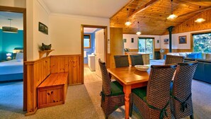 A cozy room with a wooden dining table, wicker chairs, and a bench. There is a window with a view of trees and a door leading to another room. - Freycinet Hideaway (Coles Bay)