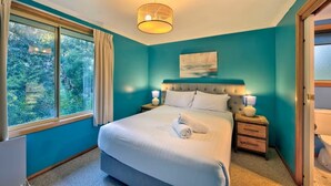 A bedroom with a large bed, two bedside tables with lamps, a window with curtains, and a painting on the wall. - Freycinet Hideaway (Coles Bay)