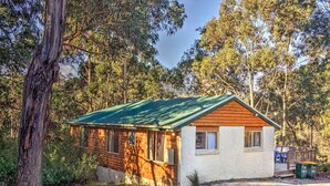 A small wooden cabin with a green roof, surrounded by dense forest. - Freycinet Hideaway (Coles Bay)