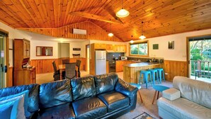 A cozy cabin interior with a wooden ceiling, a dining area, a kitchen, and a living room with a leather sofa and a white couch. - Freycinet Hideaway (Coles Bay)