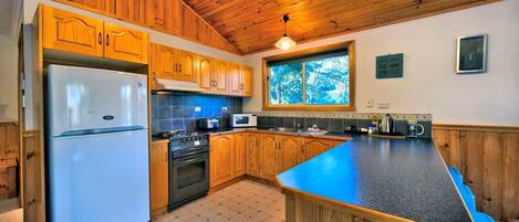 Una cocina con gabinetes de madera, refrigerador, estufa, microondas y una isla grande con taburetes.