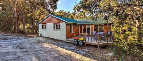 A cabin with a porch, a covered deck, and a dirt driveway.