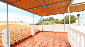 A covered terrace with terracotta tiles, white railings, and a view of the sea and greenery. - House in Puerto de Sagunto (Sagunto)
