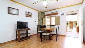 A room with a television on a wooden stand, a dining table with chairs, and a stone wall. - House in Puerto de Sagunto (Sagunto)