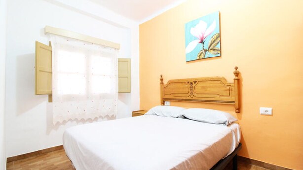 A bedroom with a wooden bed, a window with shutters, and a painting on the wall. - House in Puerto de Sagunto (Sagunto)
