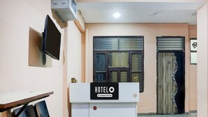 A hotel reception area with a reception desk, a TV mounted on the wall, a window with blinds, and a door with a decorative curtain. - Super Hotel O Sheetla Colony (Gurugram)