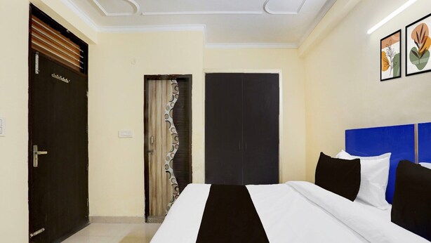 A hotel room with a large bed, a dark door, a curtain, and a blue headboard. - Super Hotel O Sheetla Colony (Gurugram)