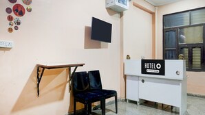 A hotel reception area with a desk, a chair, a television, and wall decorations. - Super Hotel O Sheetla Colony (Gurugram)