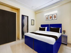 Ein Schlafzimmer mit einem großen Bett, einer Tür, einem kleinen Tisch mit einer Vase und gerahmten Kunstwerken an der Wand.