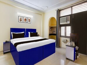 Ein Hotelzimmer mit einem großen Bett, einem Nachttisch, einem kleinen Tisch mit Tassen und einem Fenster mit Jalousien.