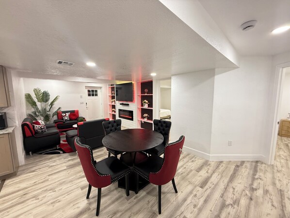 A modern living room with a dining area, featuring a round table and red chairs, a TV mounted on the wall, and a fireplace. - Spacious 3BR/2.5BA • 10 min to DIA• Private Entry (Denver)