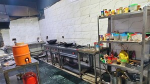 Een keuken met een fornuis, potten, een plank met bakjes en een betegelde spatwand.