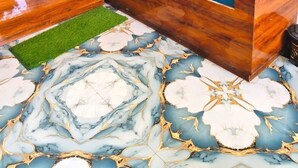 Een blauwe gestoffeerde bank met een houten onderstel, een groen vloerkleed en een vloer met een marmerprint.