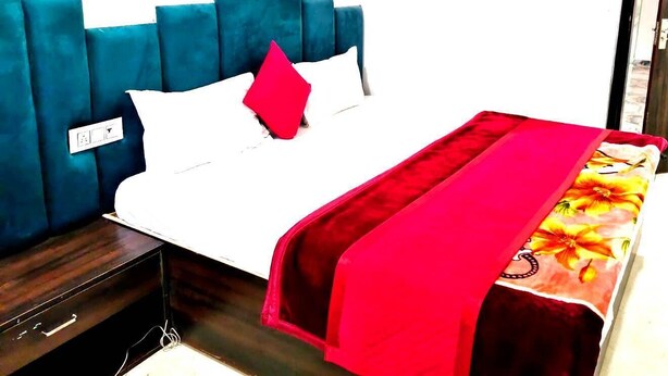 Een bed met een blauw hoofdeinde, witte beddengoed en een rood kussen.