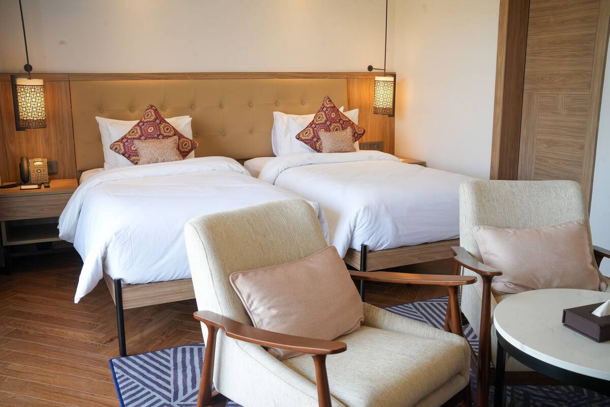 A hotel room with two beds, a round table, two armchairs, and a telephone on a nightstand.