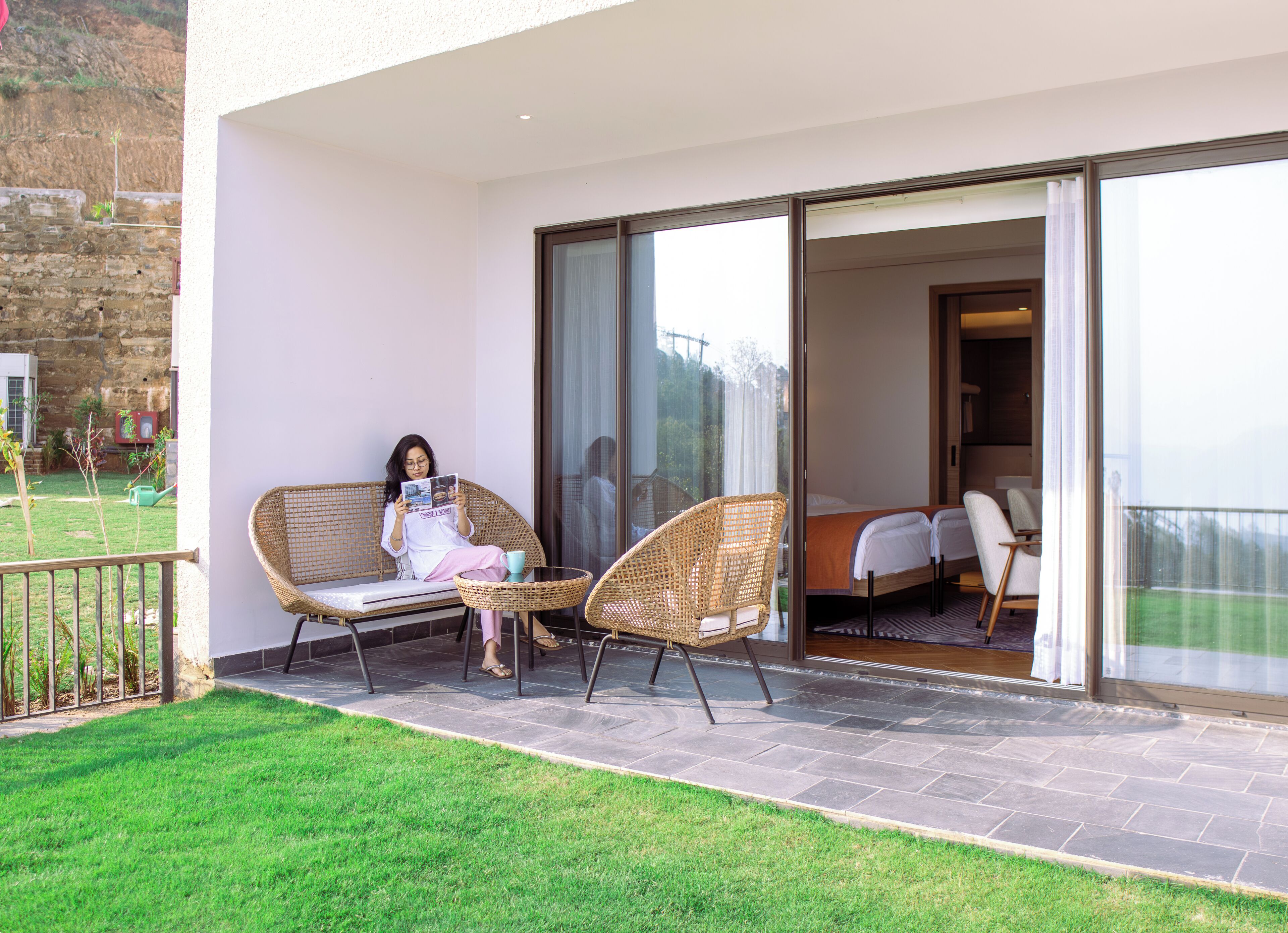 A balcony with wicker chairs, a person reading a magazine, and a view of the interior.