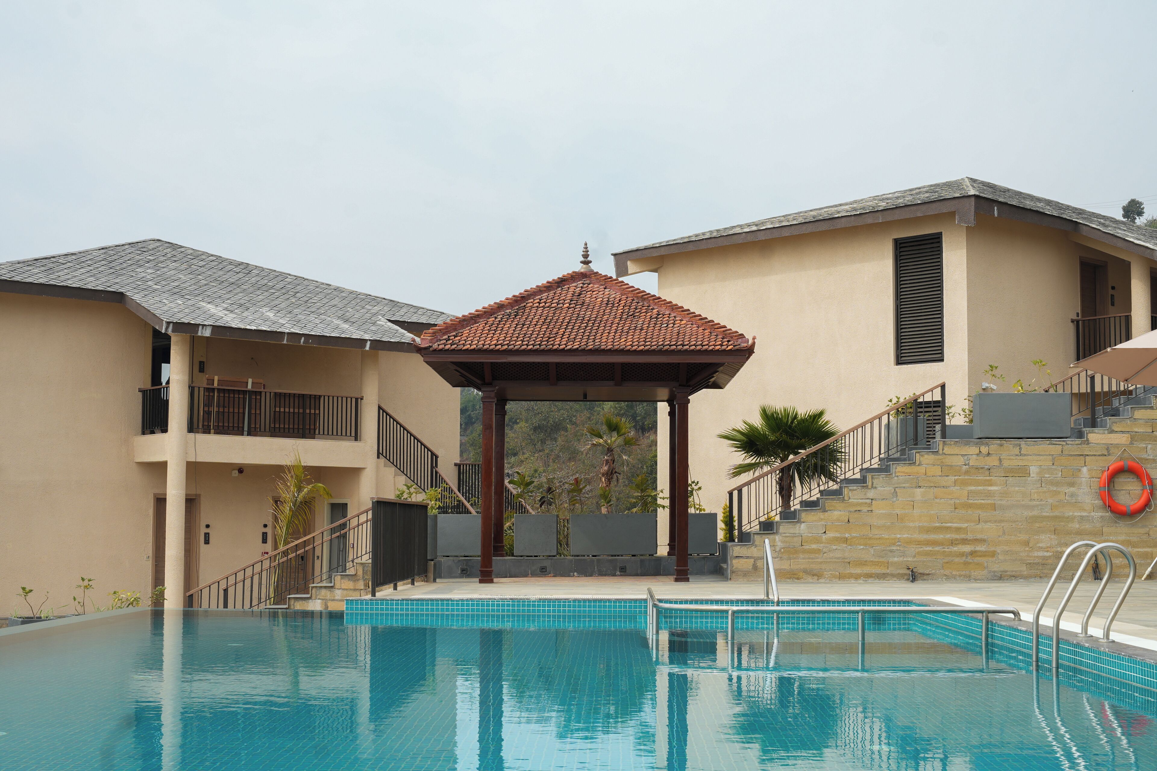A swimming pool with a gazebo, a lifebuoy, and a staircase leading to a building with a tiled roof.