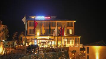 Un hotel con una entrada bien iluminada, varias banderas y un coche aparcado fuera.