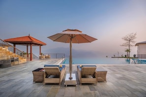 Een zwembadgedeelte met rieten meubilair, een pergola en uitzicht op zee.