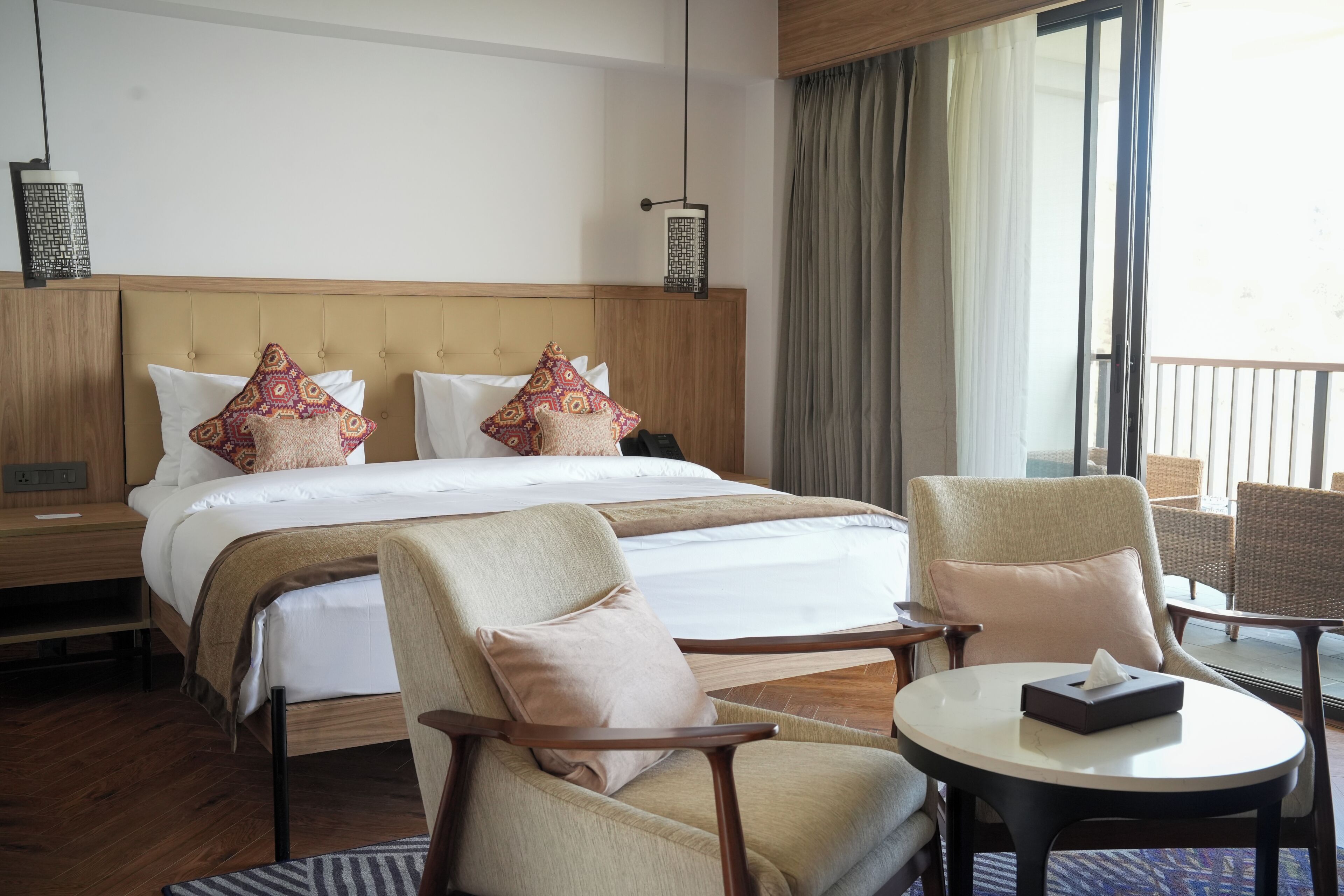 Une chambre d’hôtel avec un grand lit, deux chaises, une petite table et un balcon avec des rideaux.