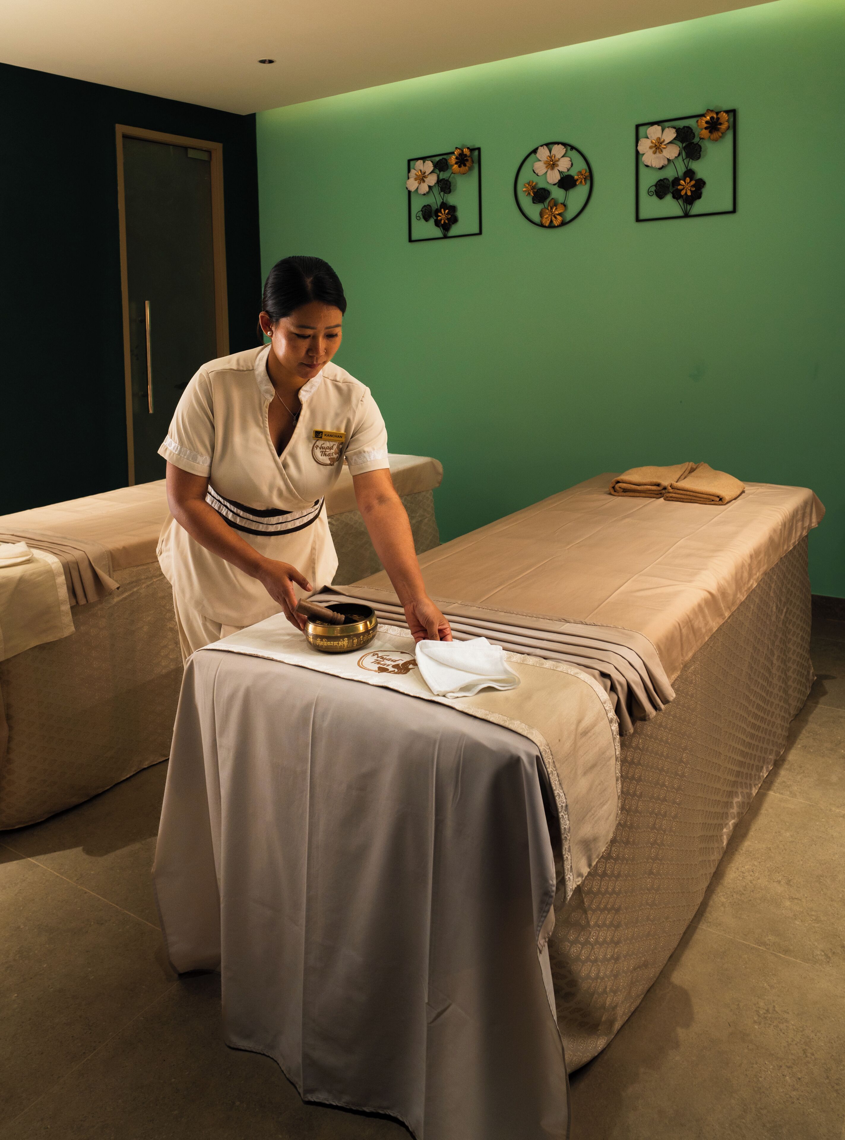 Een massageruimte met twee bedden, een massagetafel en een wand met bloemversiering.