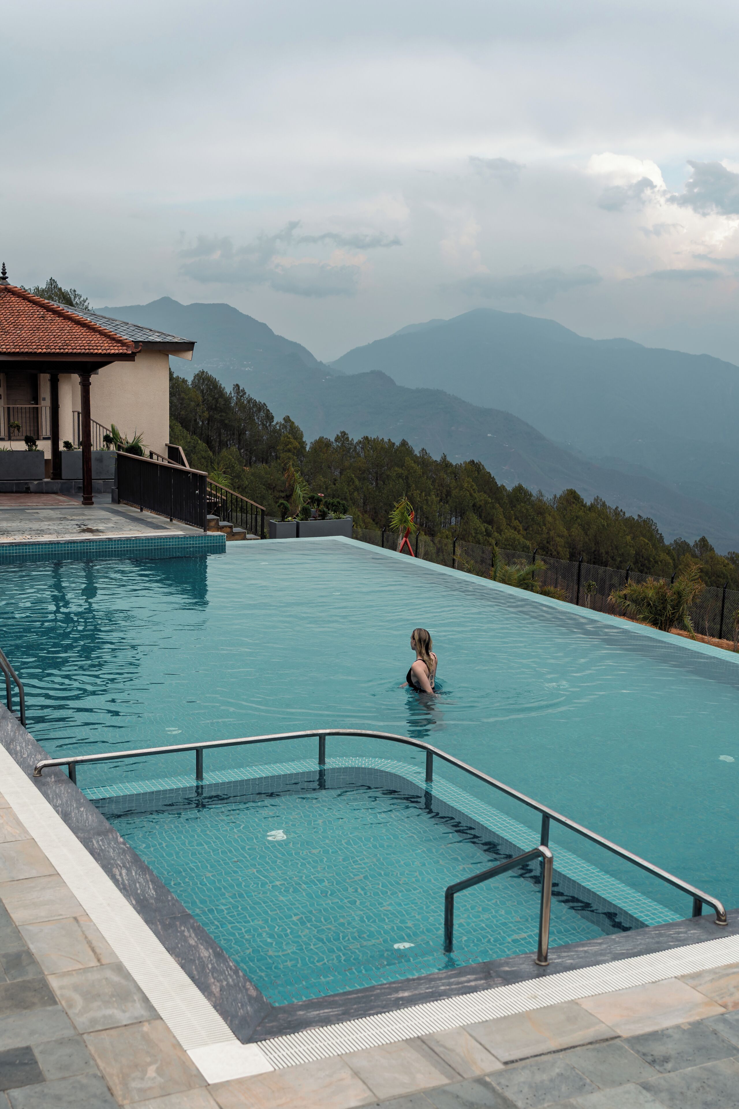 A swimming pool with a view of mountains, a building with a tiled roof, and a person swimming.