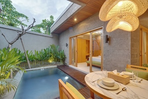 A modern outdoor pool area with a wooden deck, a dining table set with plates and glasses, and a large woven light fixture. - Villa Umahera - Canggu (Canggu)