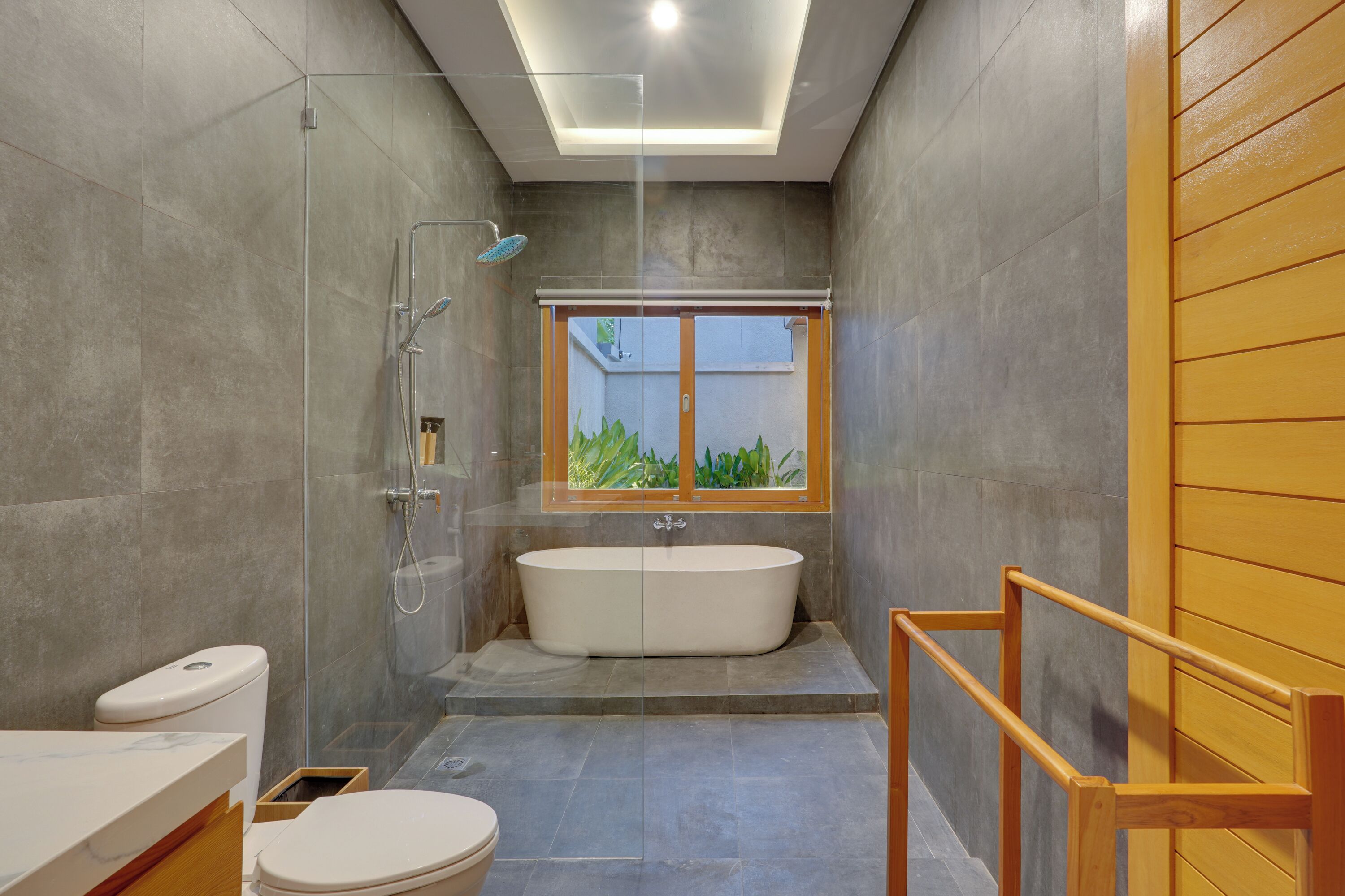 Une salle de bain moderne avec une baignoire sur pieds, une douche à l’italienne et une fenêtre donnant sur un espace verdoyant.
