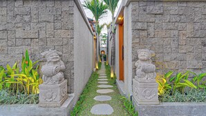 A stone pathway flanked by statues and plants, leading to a building with a traditional roof. - Villa Umahera - Canggu (Canggu)