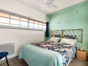 A bedroom with a bed, a chair, a window, a ceiling fan, and a nightstand with a candle. - The Big Blue! Between sea and mountains (Saint-Cyprien)