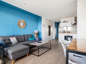 A modern living room with a grey sectional sofa, a coffee table, and a dining area with a wooden table and white chairs. - The Big Blue! Between sea and mountains (Saint-Cyprien)