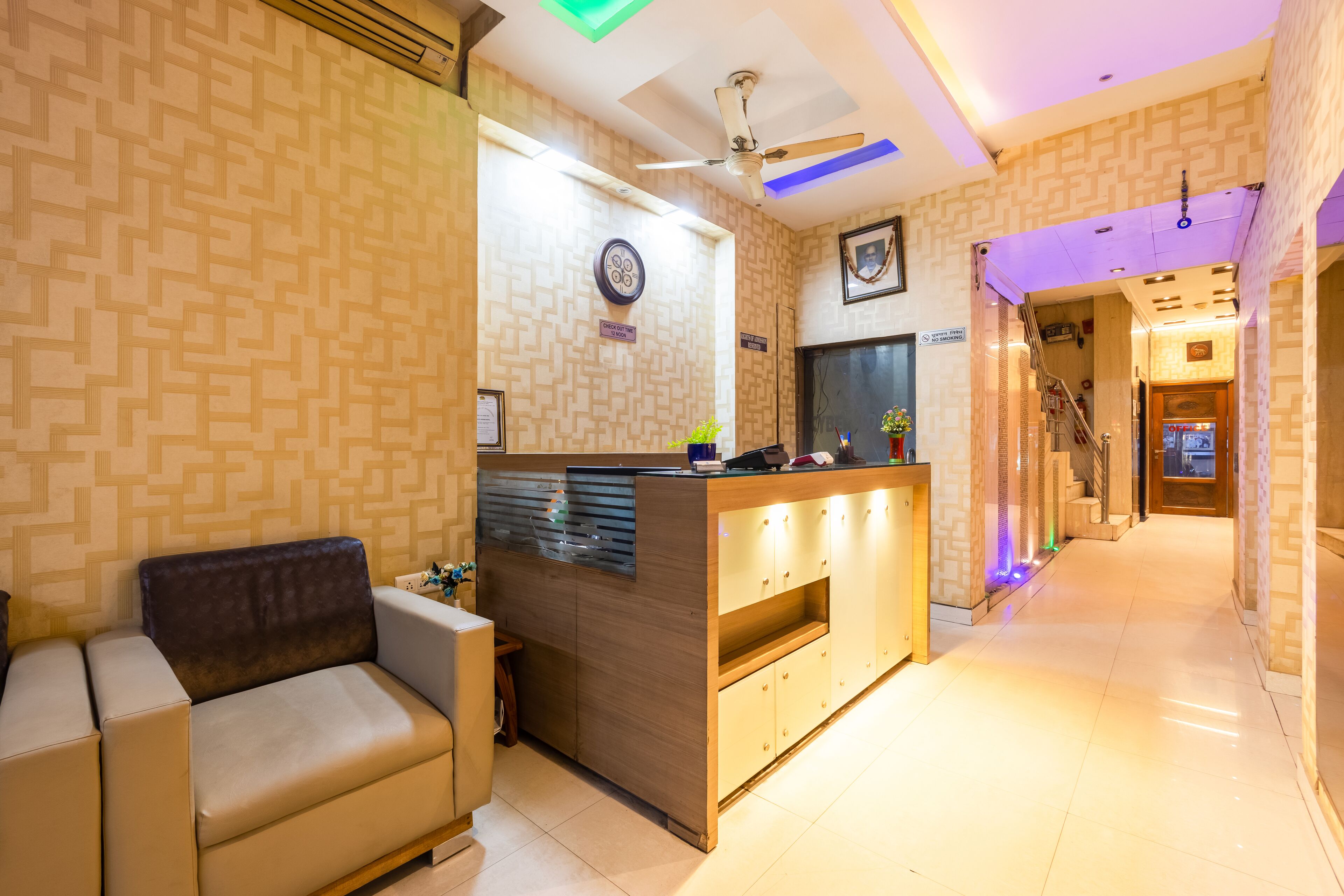 A modern hotel lobby with a reception desk, a sofa, and a staircase leading to other areas.