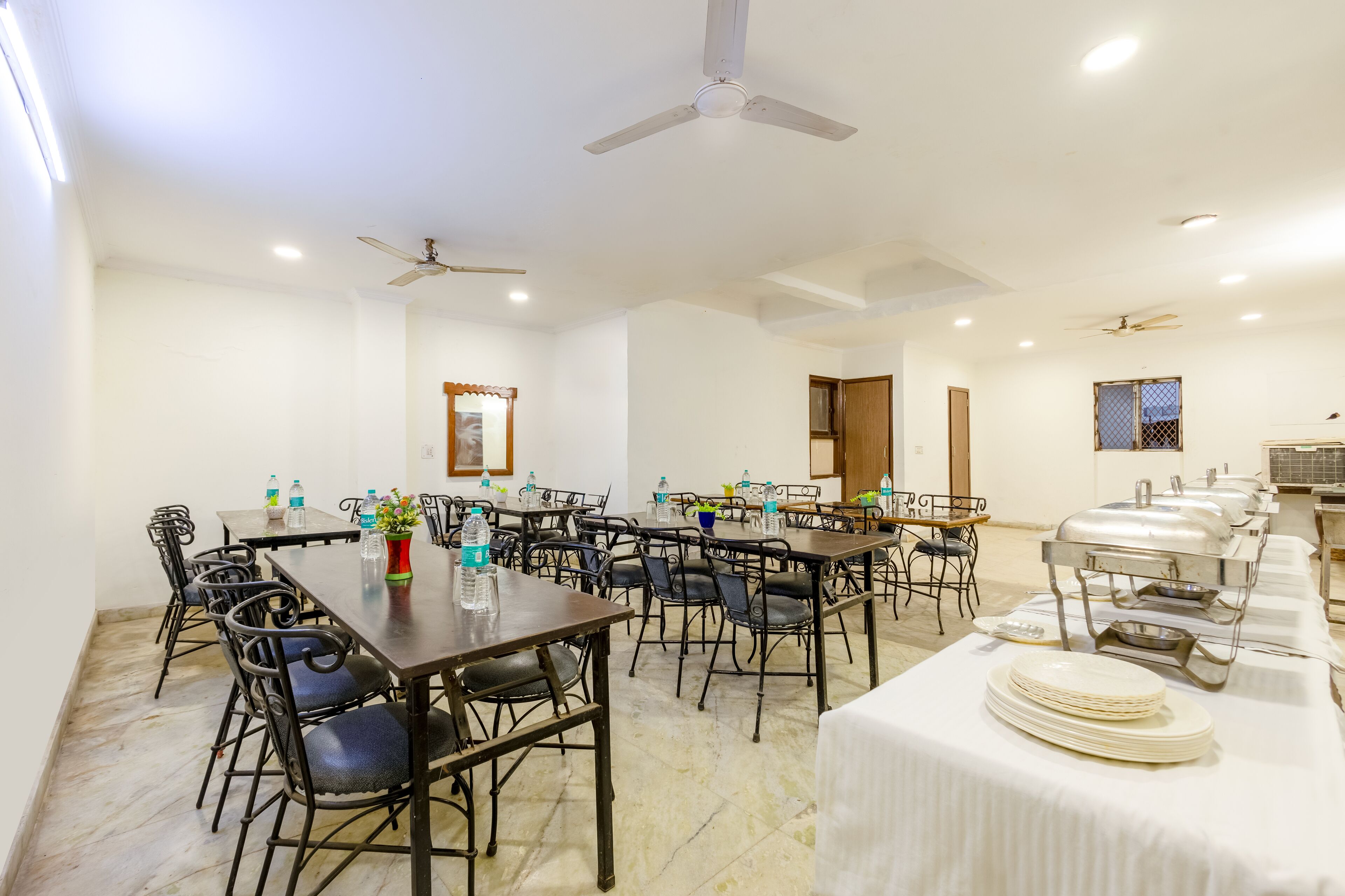 A conference room with multiple tables, chairs, ceiling fans, and a buffet setup.
