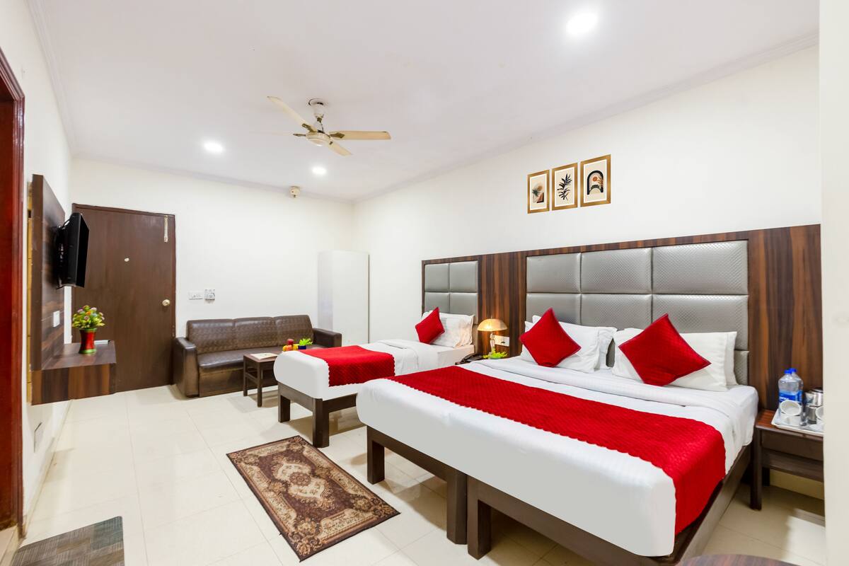 Quarto de hotel com duas camas, um sofá, uma televisão e um ventilador de teto.
